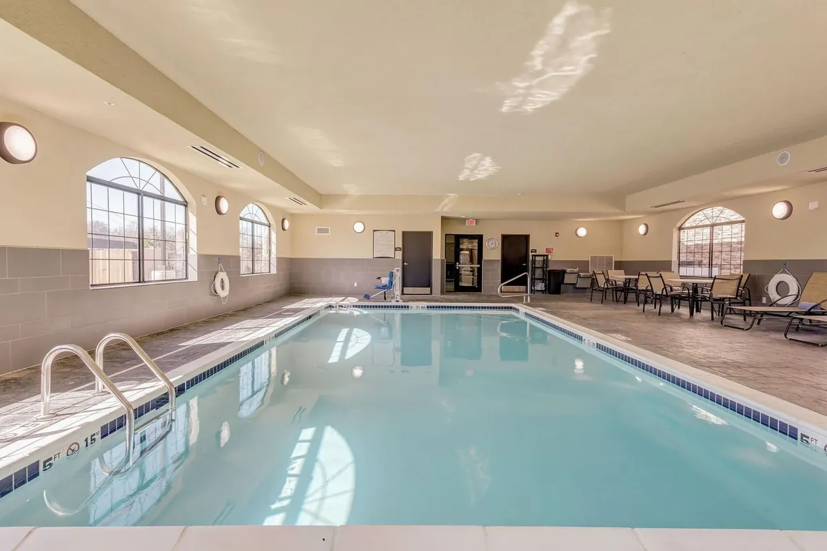 This image shows an inviting indoor swimming pool area with comfortable lounge chairs and expansive windows that allow natural light to flood the space. The scene suggests opportunities for gentle exercise, relaxation, and socializing, all within a tranquil and well-maintained setting.