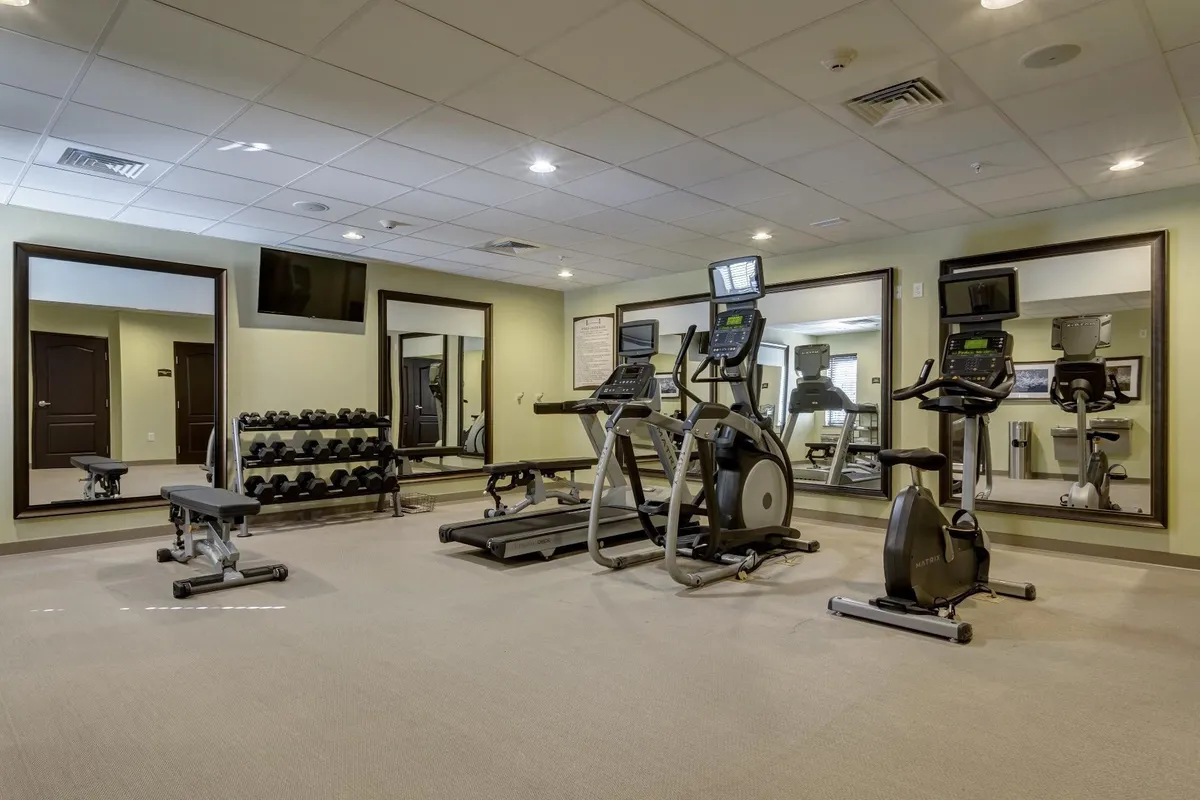 A motivating fitness center filled with modern exercise equipment, mirrors, dumbbells, and television screens. The space is bright and spacious, inviting guests to engage in a variety of fitness routines or group workouts.