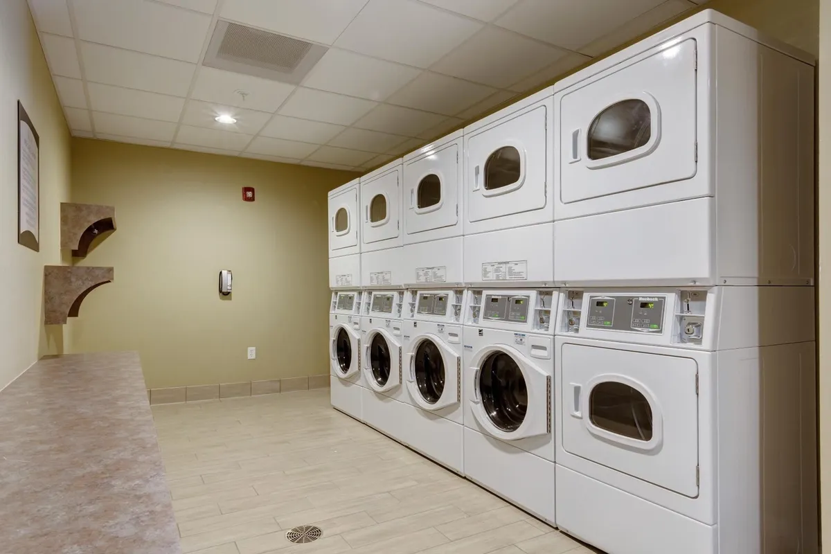 A practical, modern laundry room equipped with washing machines, dryers, and counter space for folding clothes. The environment is clean, efficient, and easy to access for guests on extended stays.