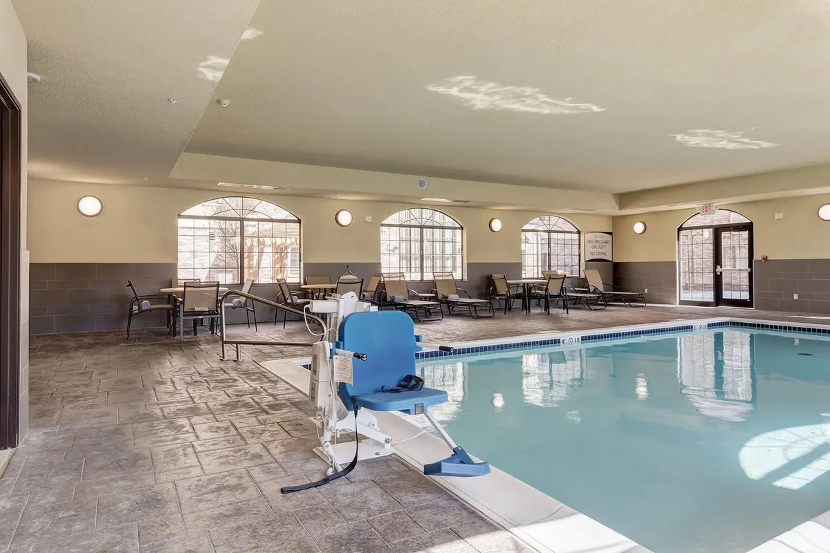 A tranquil indoor pool area with accessibility features, lounge chairs, and large windows letting in natural light. The setting is serene, ideal for relaxing swims, social interactions, or quiet reflection after a busy day.