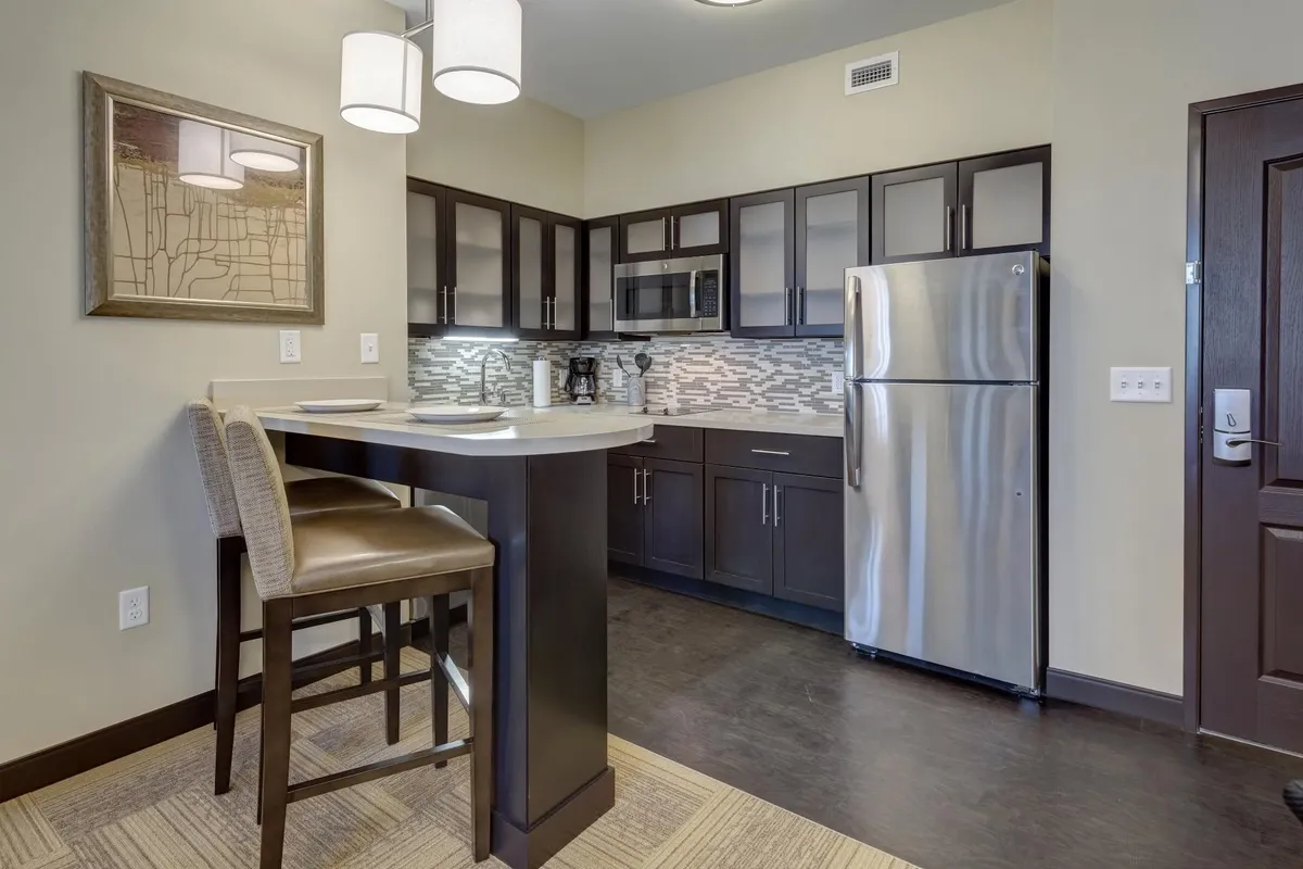 A stylish, modern kitchen featuring a central island with bar stools, stainless steel appliances, and decorative backsplash tiles. The open layout is perfect for preparing meals, entertaining, or enjoying a casual breakfast.