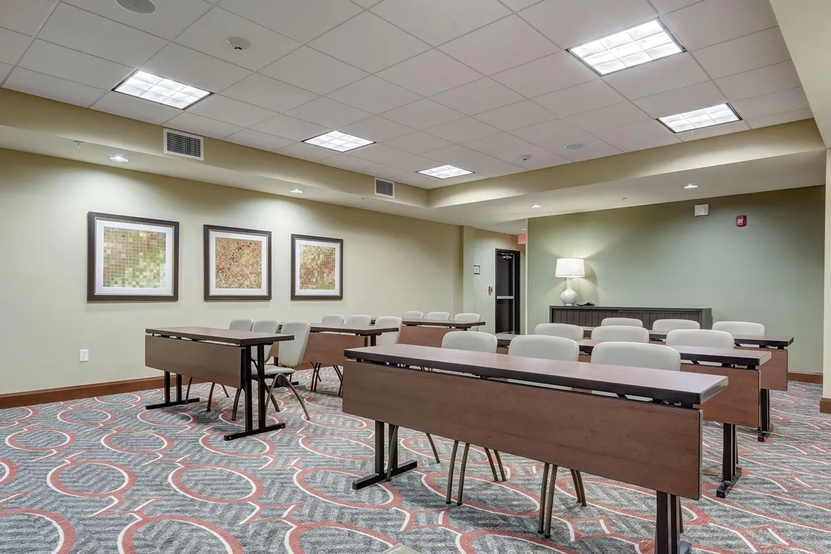 A modern workspace featuring rows of desks arranged to encourage productivity, accented by framed artwork and stylish flooring. The setup is designed for business meetings, focused work, and collaborative sessions, creating a professional yet inviting atmosphere.
